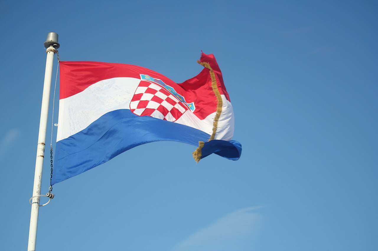 Croatian national flag flying from a pole against a blue sky